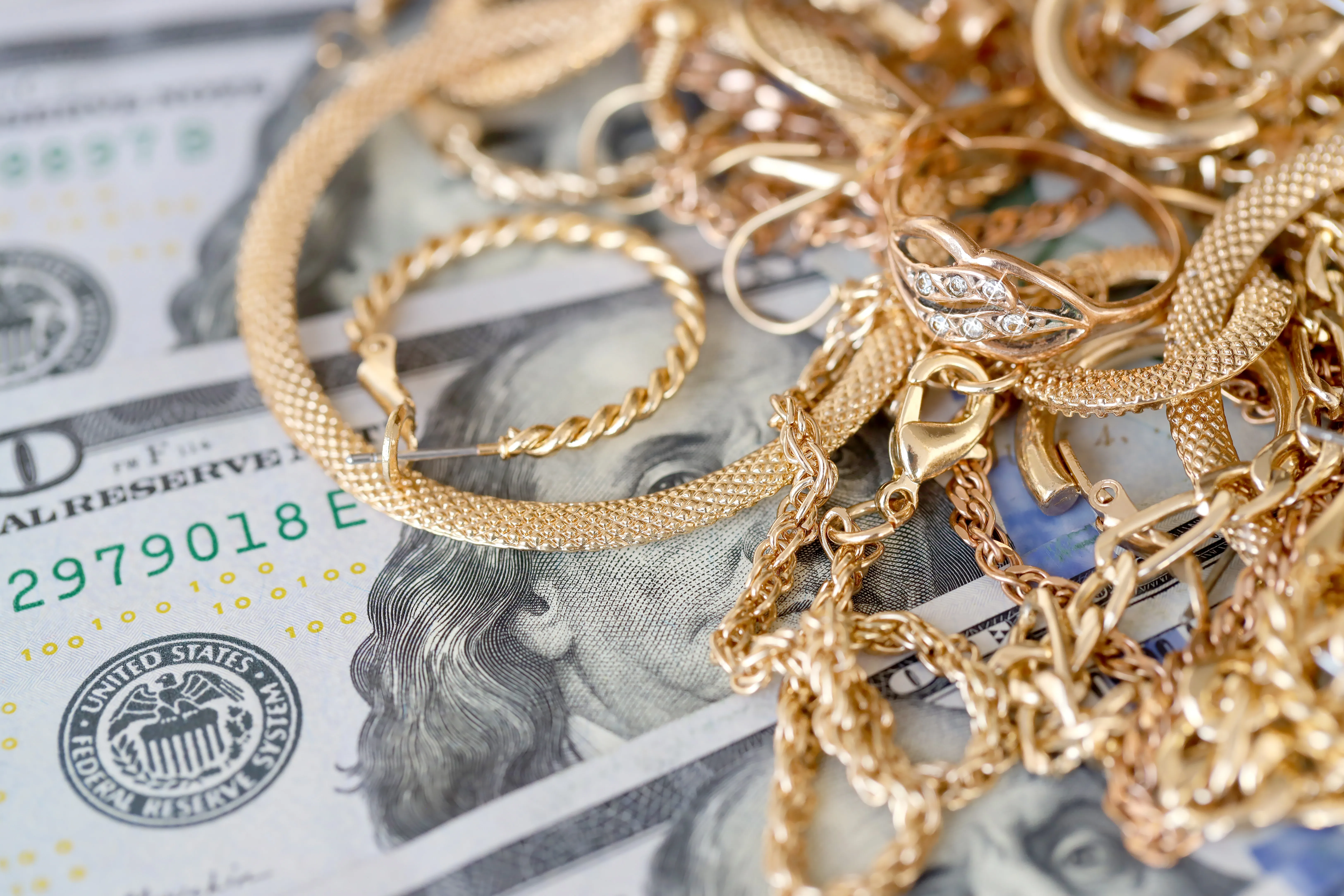 Gold jewelry pieces scattered over U.S. dollar bills, showcasing luxury and wealth. Visit Monarch Jewelry for fine pieces.