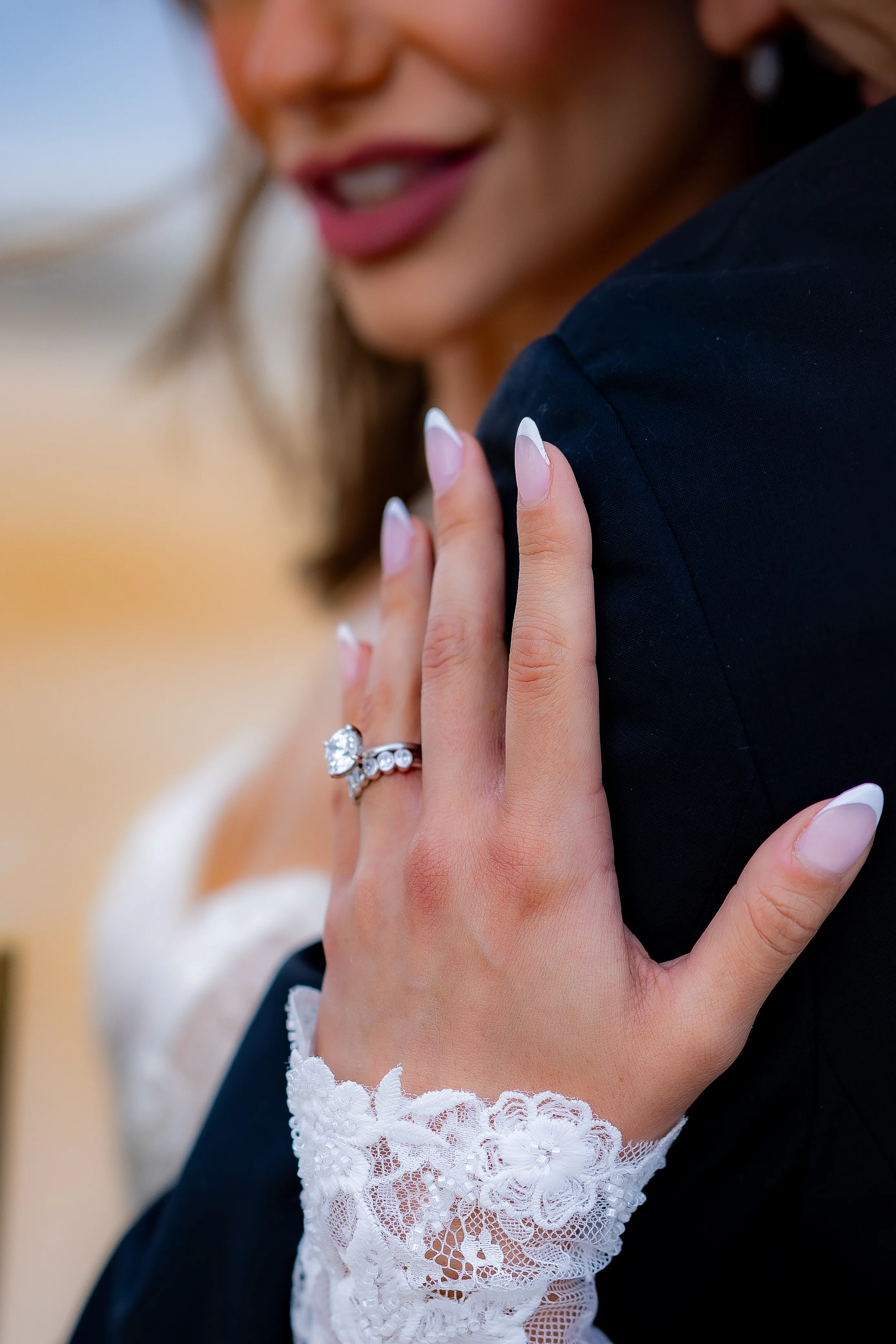 A bride shows off her engagement ring while embracing her groom, highlighting love and joy. Visit Monarch Jewelry for rings.