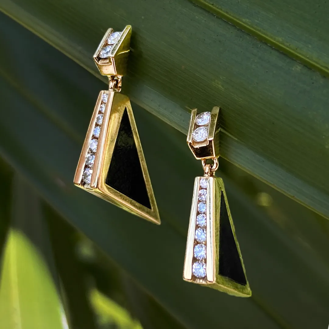 Gold and black triangle earrings with diamonds, displayed against green foliage. Click to shop estate jewelry at Monarch Jewelry