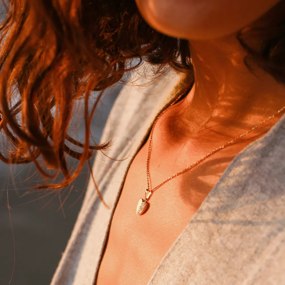 Close-up of a woman wearing a delicate gold necklace with a heart pendant, showcasing elegant jewelry.