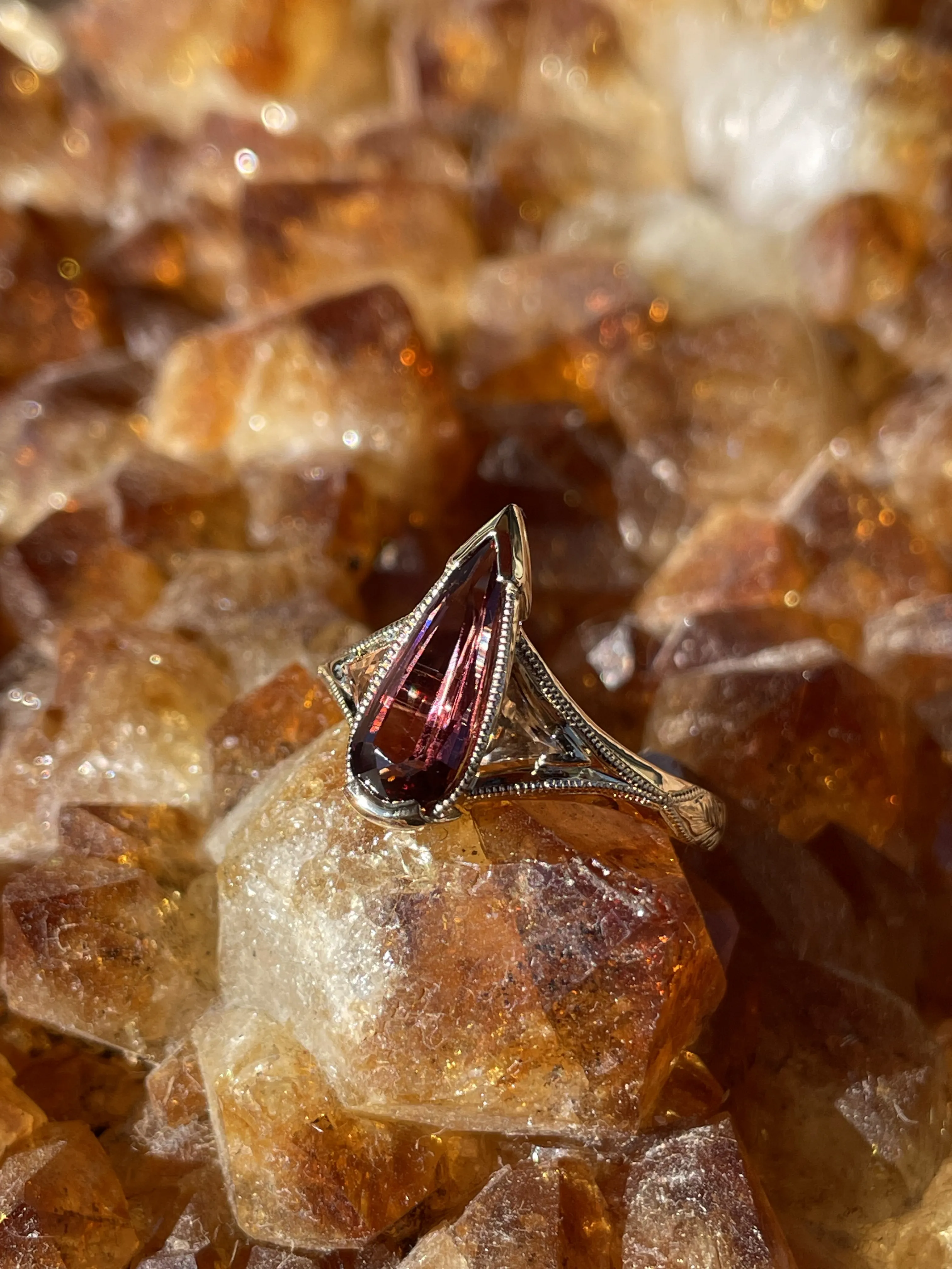 Elegant silver ring with a pear-shaped pink gemstone, resting on sparkling amber crystals. Visit Monarch Jewelry in Winter Park.