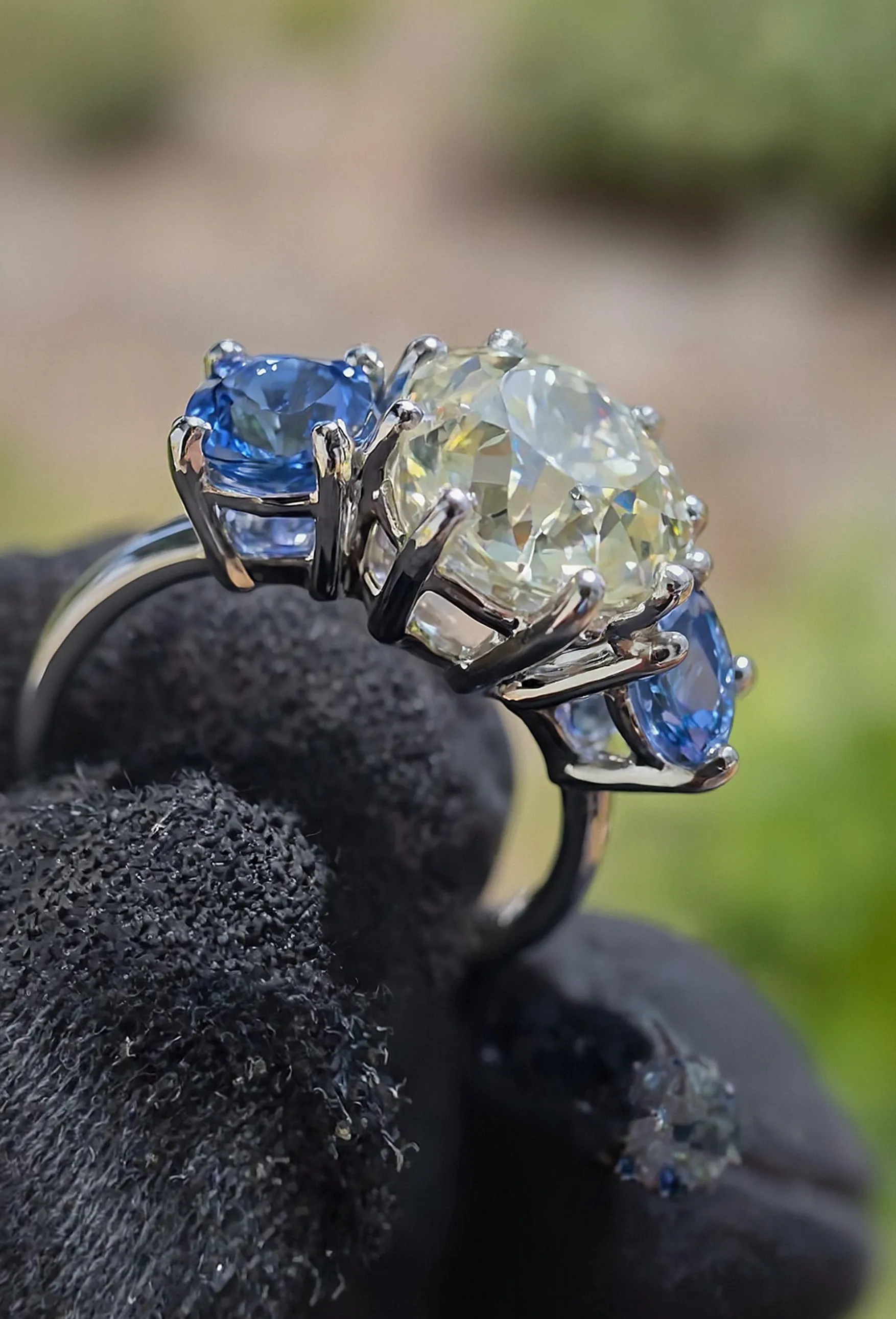 Elegant three-stone ring featuring a large center diamond flanked by two blue gemstones, held in a silver setting.