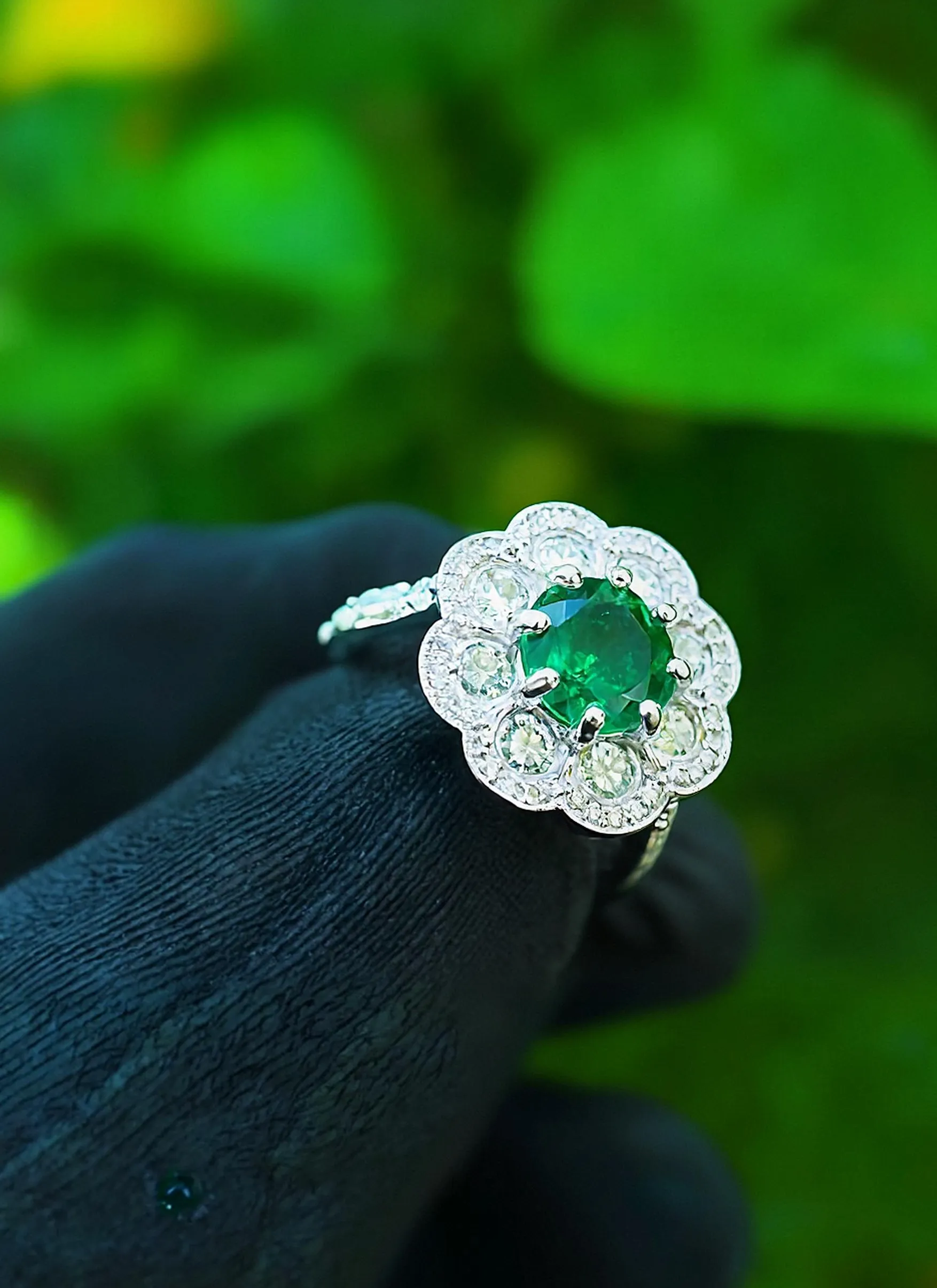 Emerald and diamond flower ring held in a gloved hand, showcasing fine jewelry from Monarch Jewelry in Winter Park.