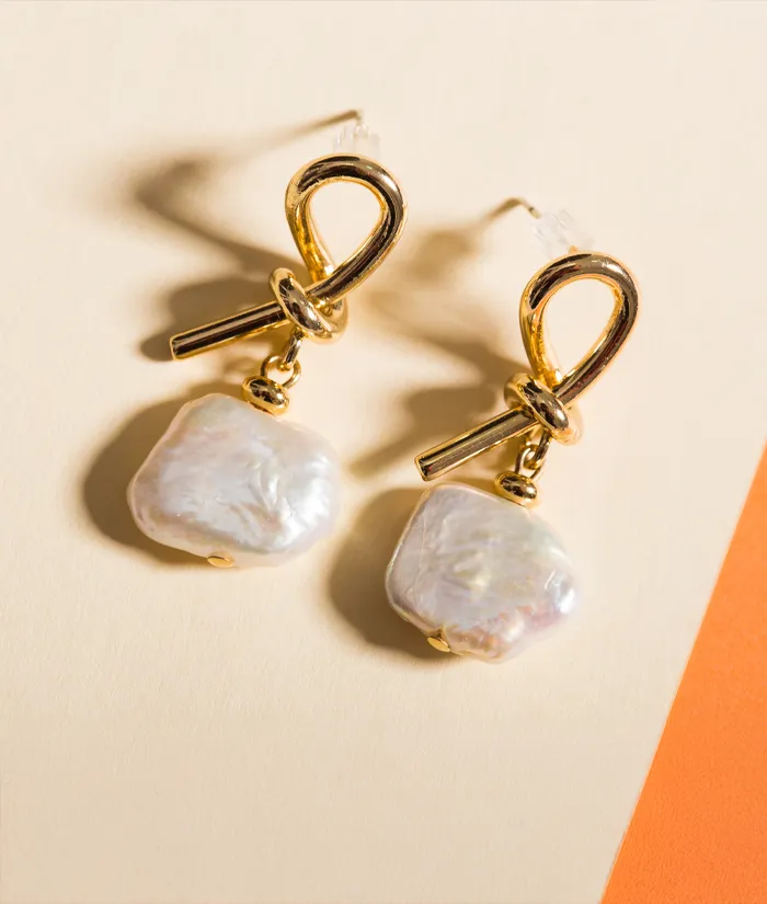 Gold earrings with pearl drops on a soft background. Click to view store information at Monarch Jewelry in Winter Park.