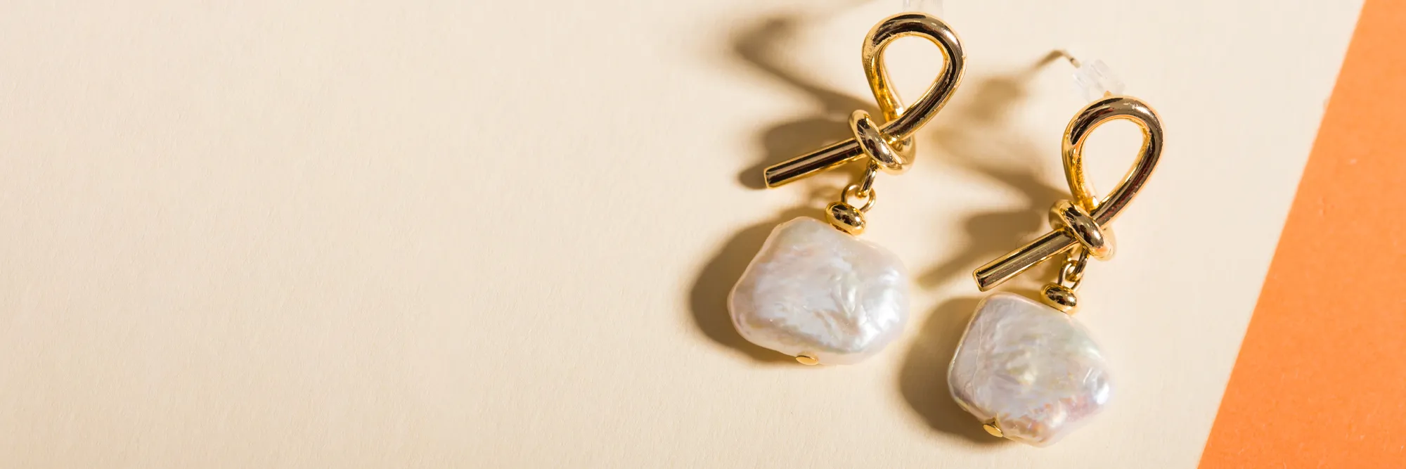 Gold earrings with pearl drops on a soft background. Click to view store information at Monarch Jewelry in Winter Park.