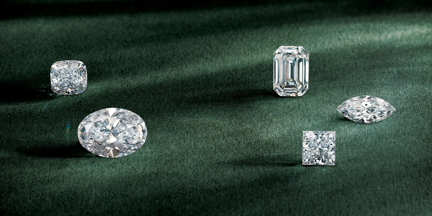 Five sparkling diamonds of various cuts displayed on a green surface, showcasing elegance and luxury. Visit Monarch Jewelry.