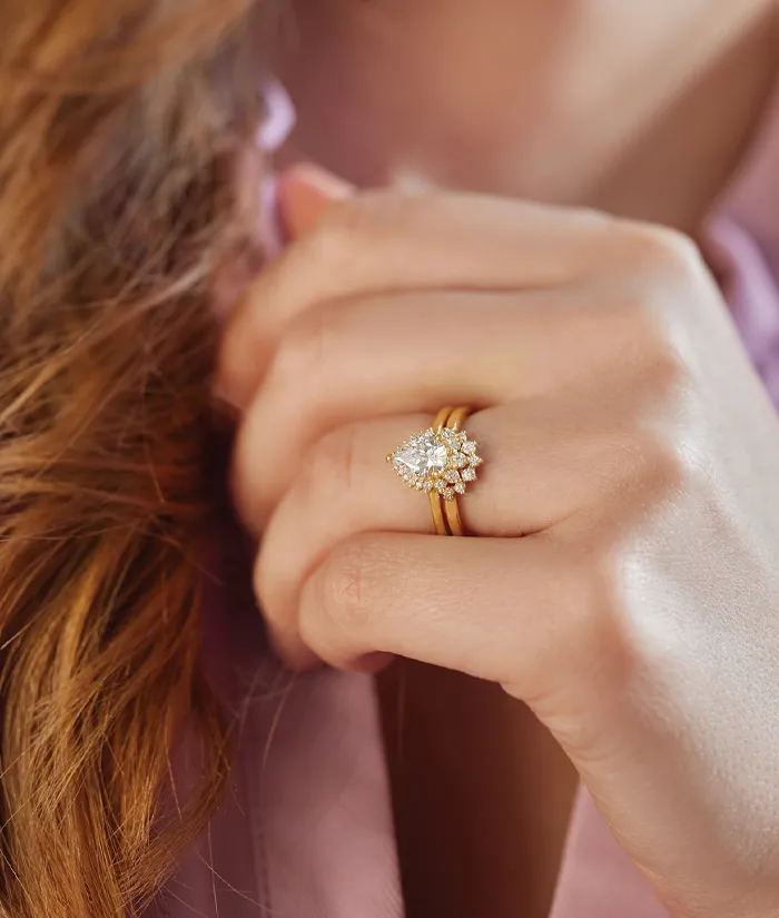 Elegant gold engagement ring with a pear-shaped diamond centerpiece, worn on a woman's hand. Visit Monarch Jewelry for details.