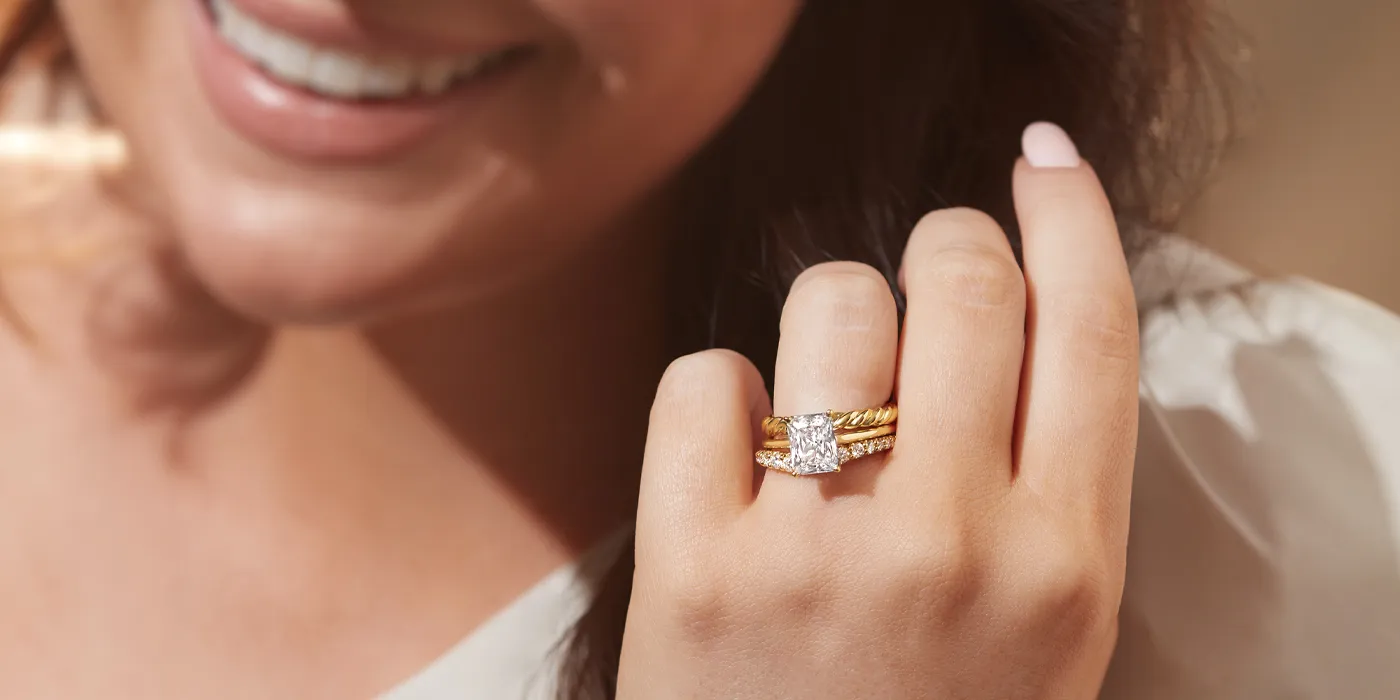 Woman smiling, showcasing a diamond engagement ring with gold bands at Monarch Jewelry in Winter Park.
