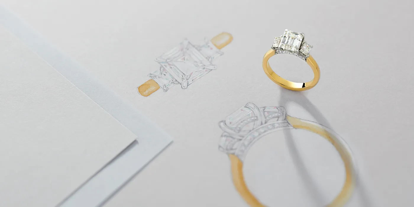 A gold engagement ring beside its sketch on paper, showcasing fine jewelry design at Monarch Jewelry in Winter Park.