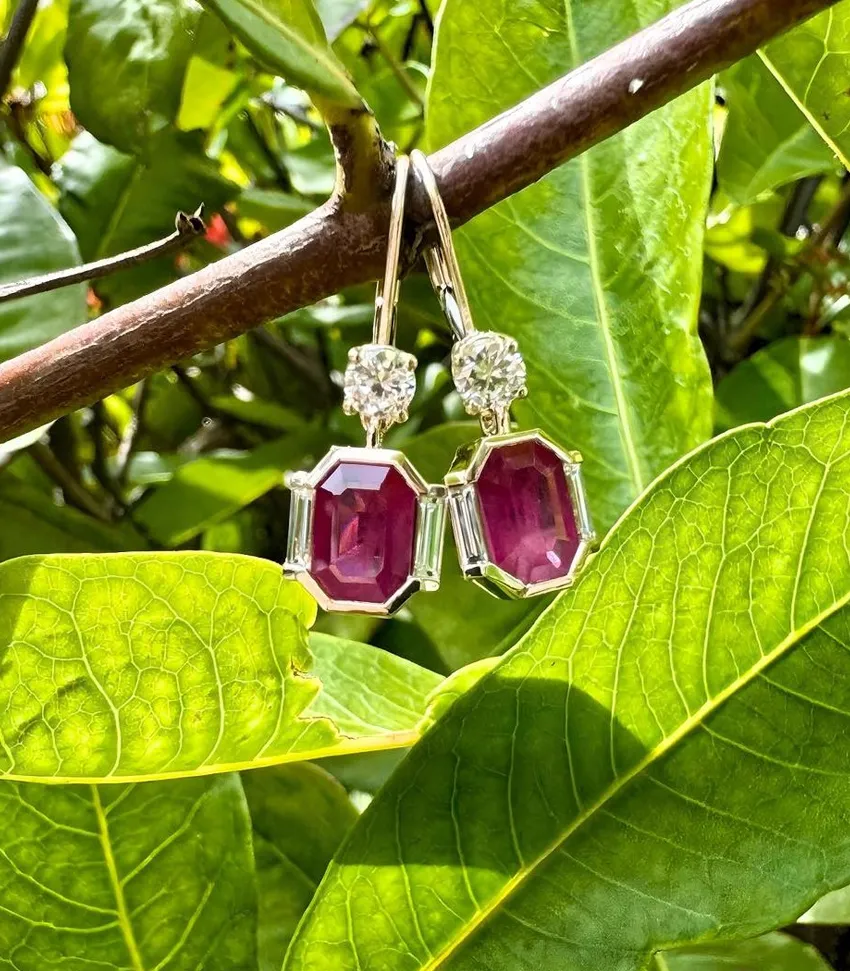 Elegant ruby earrings with diamond accents hanging on a branch among green leaves. Visit Monarch Jewelry in Winter Park.