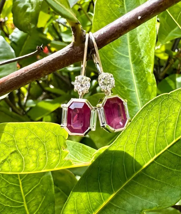 Elegant ruby earrings with diamond accents hanging on a branch among green leaves. Visit Monarch Jewelry in Winter Park.