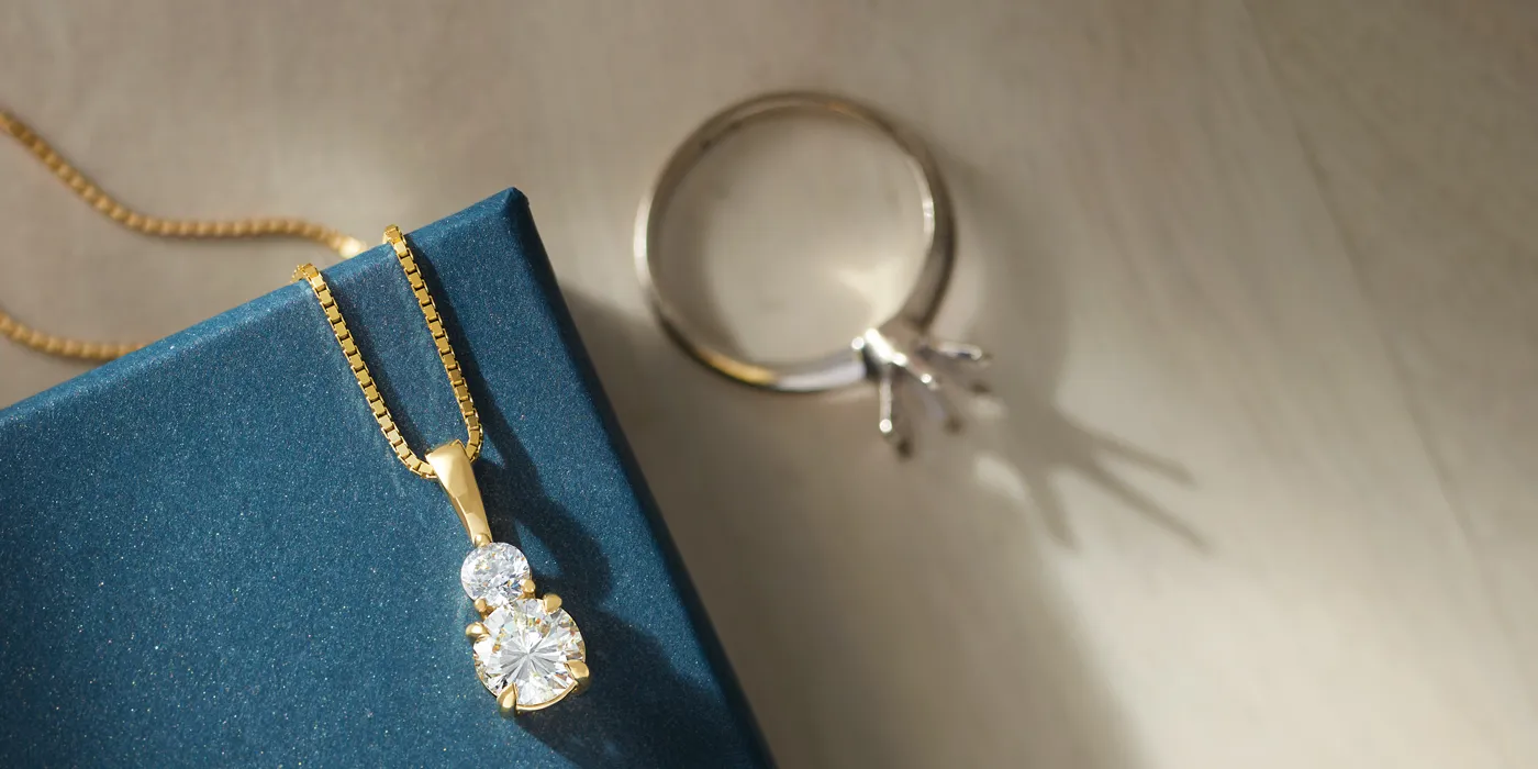 Gold necklace with a diamond pendant and a silver ring on a blue box, showcasing fine jewelry from Monarch Jewelry.