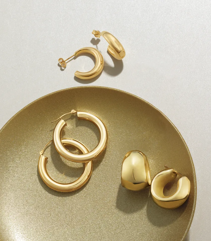 Gold hoop earrings displayed on a gold plate, featuring two pairs of different styles. Shop at Monarch Jewelry in Winter Park.