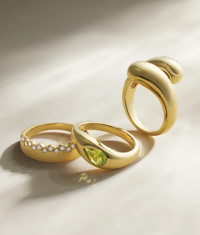 Three elegant gold rings featuring a diamond-studded band and a green gemstone, displayed on a soft surface.