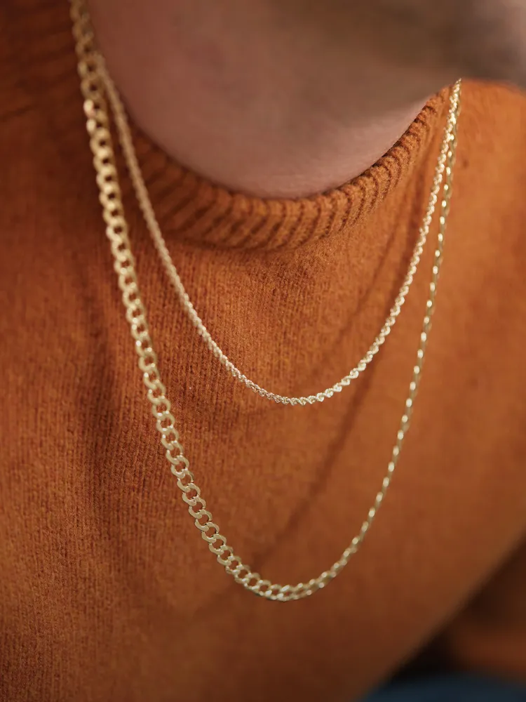 Gold chains layered over an orange sweater, showcasing elegant jewelry style. Shop Chains at Monarch Jewelry, Winter Park.