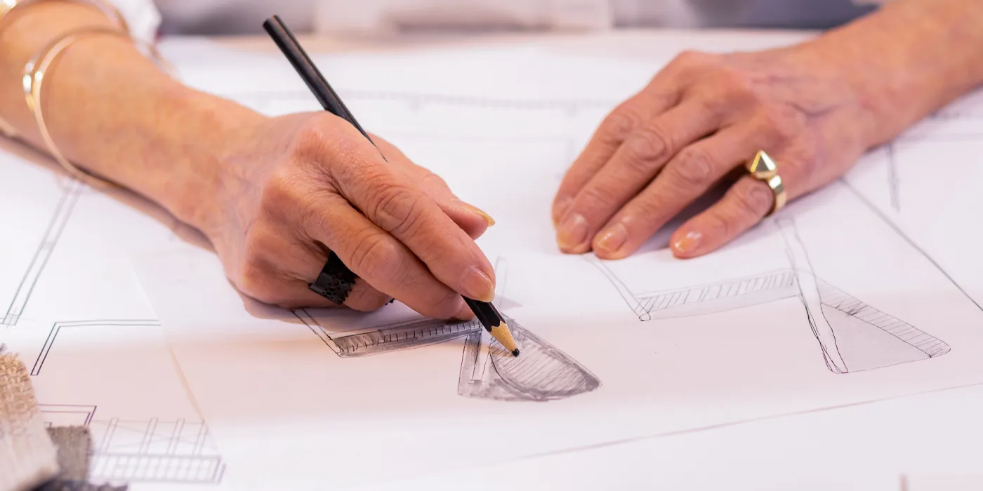 A hand sketches jewelry designs on paper, showcasing creativity and craftsmanship at Monarch Jewelry in Winter Park.