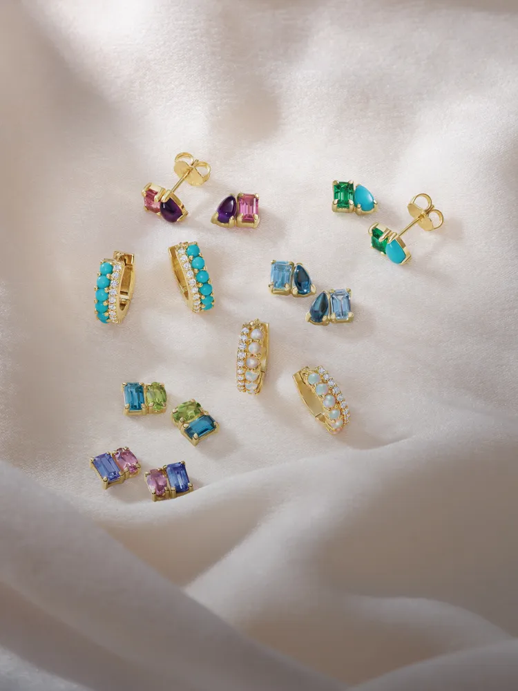 Colorful gold earrings arranged on soft fabric, showcasing various gemstones. Click to shop earrings at Monarch Jewelry.