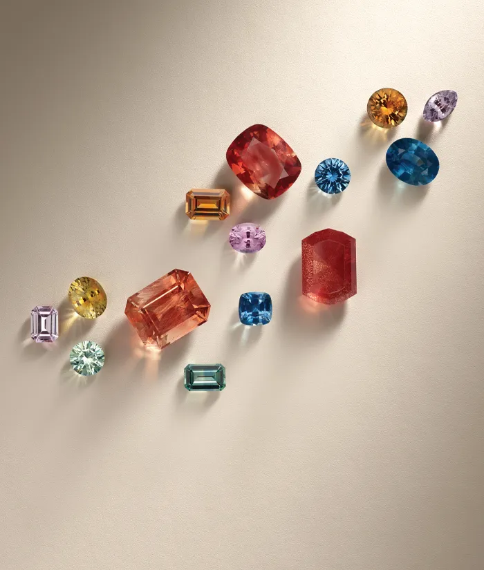 Colorful loose gemstones arranged artistically on a light background. Click to start a project at Monarch Jewelry.
