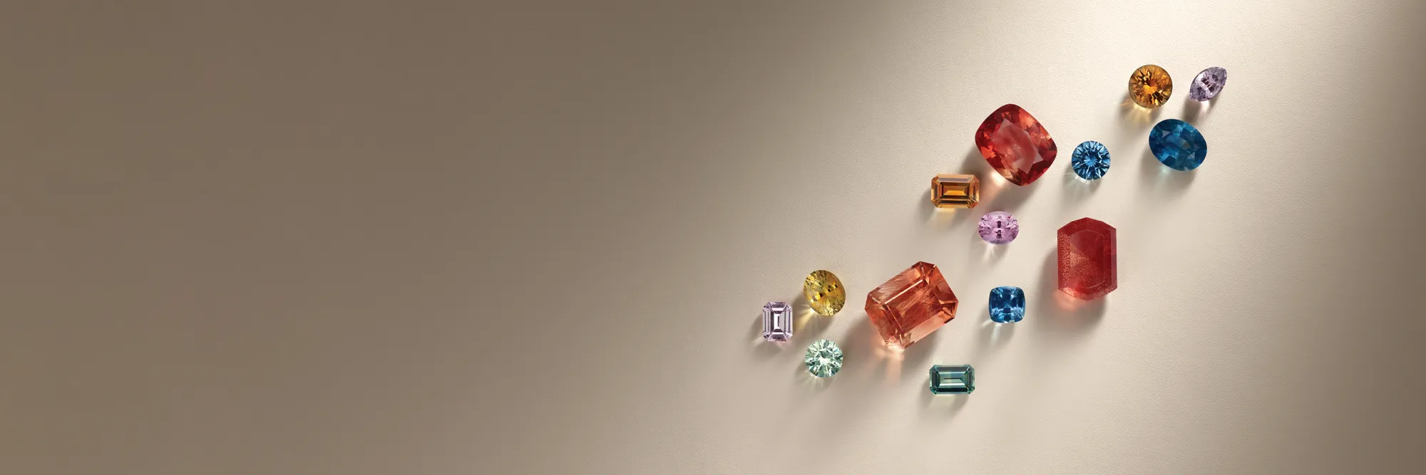 Colorful loose gemstones arranged artistically on a light background. Click to start a project at Monarch Jewelry.