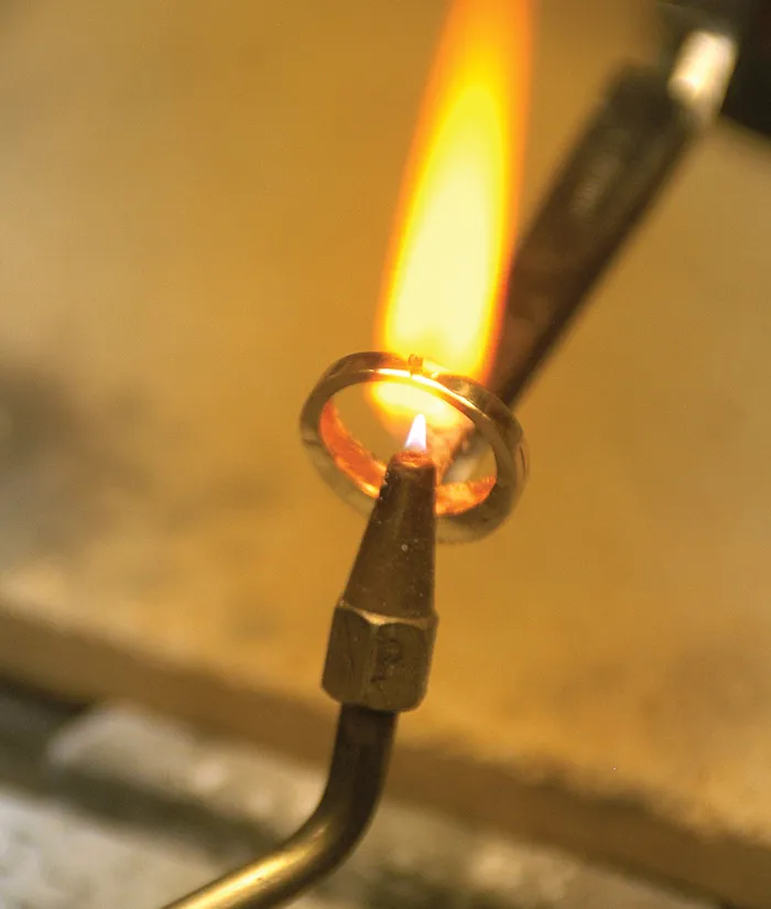 A jeweler uses a torch to heat a metal ring, creating a flame as part of the jewelry-making process.