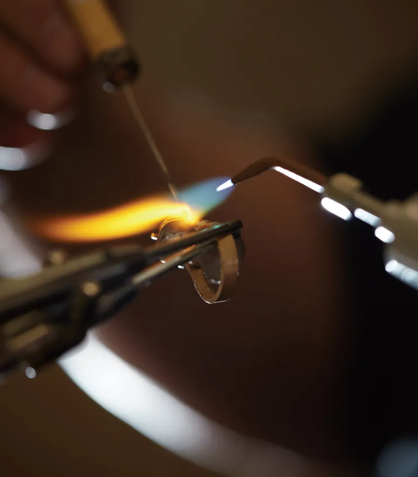 A jeweler uses a torch to heat and shape a metal ring in a workshop setting.