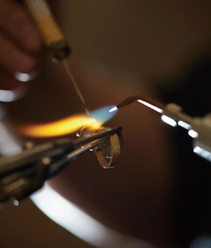 A jeweler uses a torch to heat and shape a metal ring in a workshop setting.