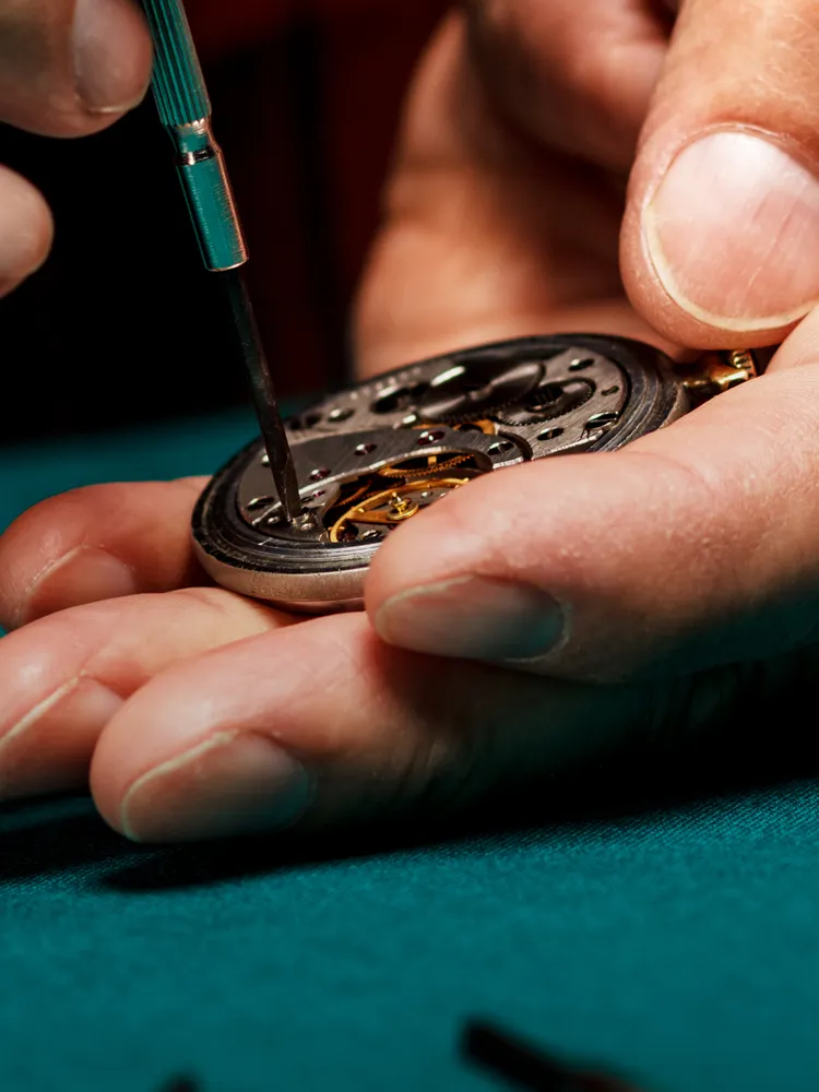 A jeweler carefully repairs a watch movement using a screwdriver, showcasing intricate craftsmanship.
