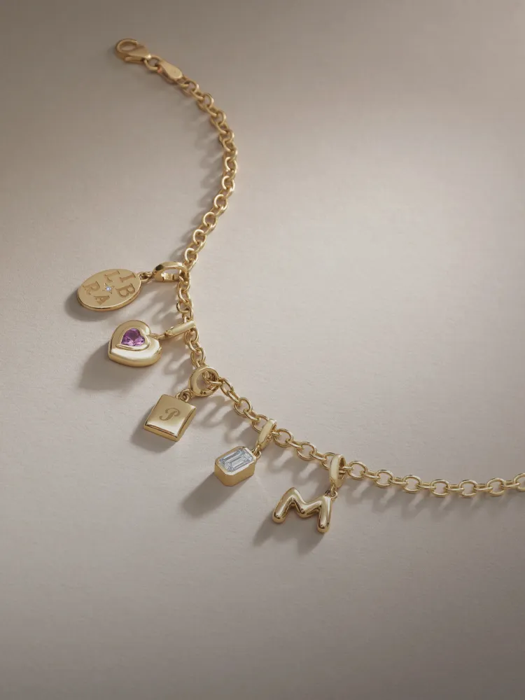 Gold charm bracelet featuring various charms including a heart, lock, and initials. Shop pendants & charms at Monarch Jewelry.