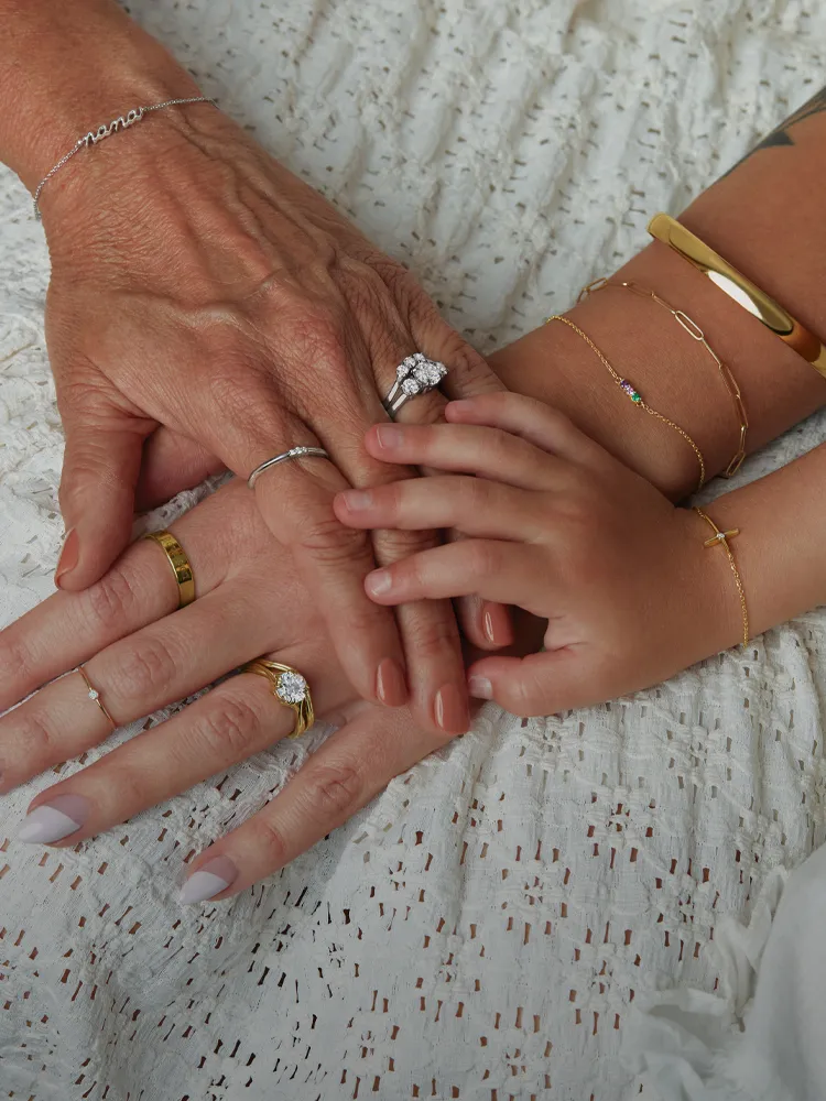 Three generations of hands with various rings and bracelets, showcasing family bonds. Shop at Monarch Jewelry, Winter Park.
