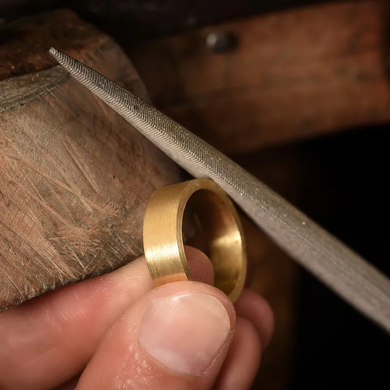 A jeweler files a gold ring, showcasing craftsmanship at Monarch Jewelry in Winter Park.