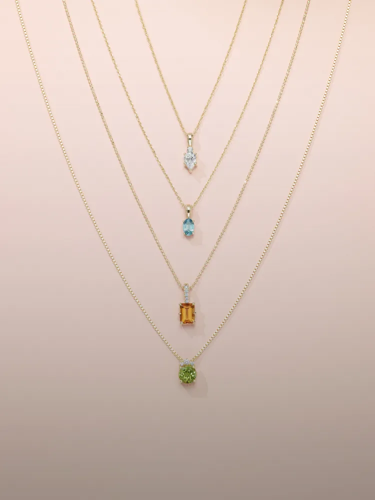 Layered gold necklaces with colorful pendants displayed on a soft background. Shop Pendants at Monarch Jewelry, Winter Park.