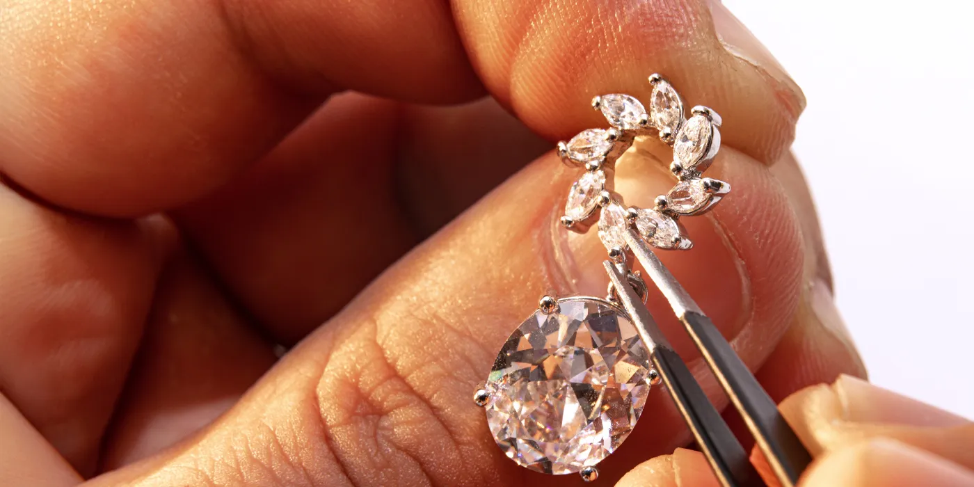 A jeweler delicately holds a diamond earring with tweezers, showcasing intricate details and craftsmanship.