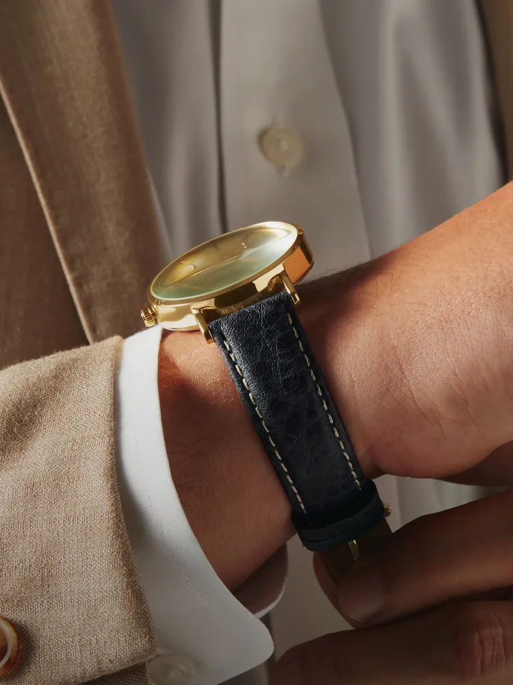 Gold watch with a blue leather strap on a man's wrist. Shop watches at Monarch Jewelry, Winter Park.