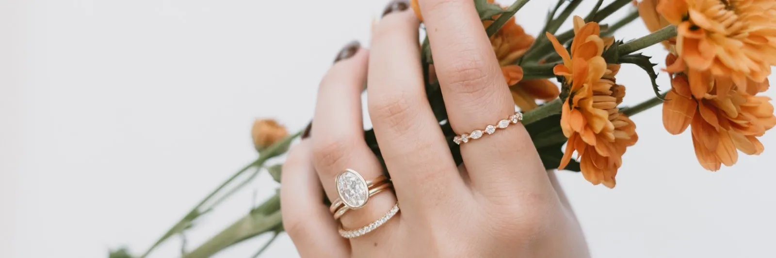 Hand wearing oval engagement ring and other rings holding orange flowers