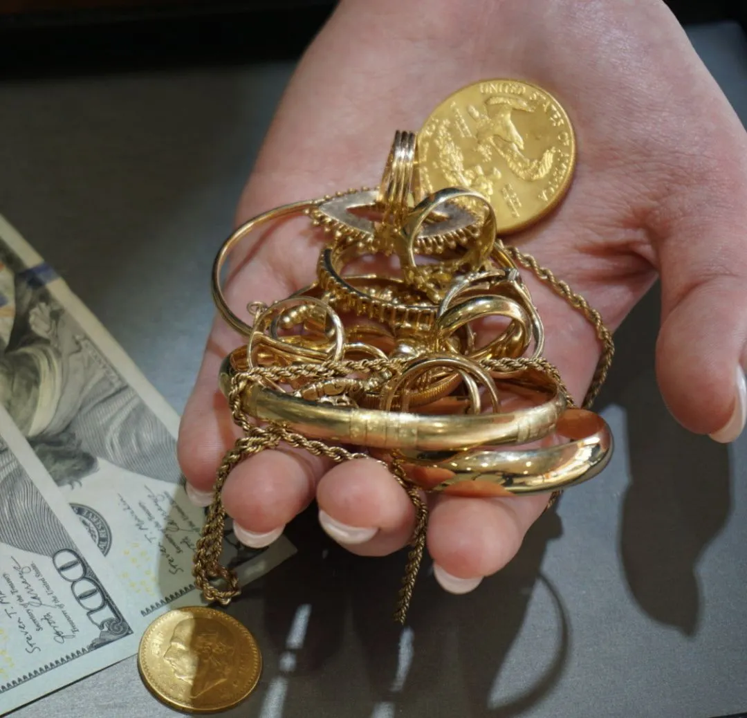 Gold jewelry and coins laying on hundred dollar bills