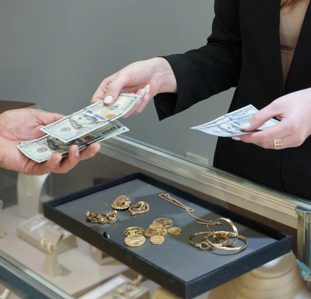 person handing hundred dollar bills to another person with a tray of gold jewelry
