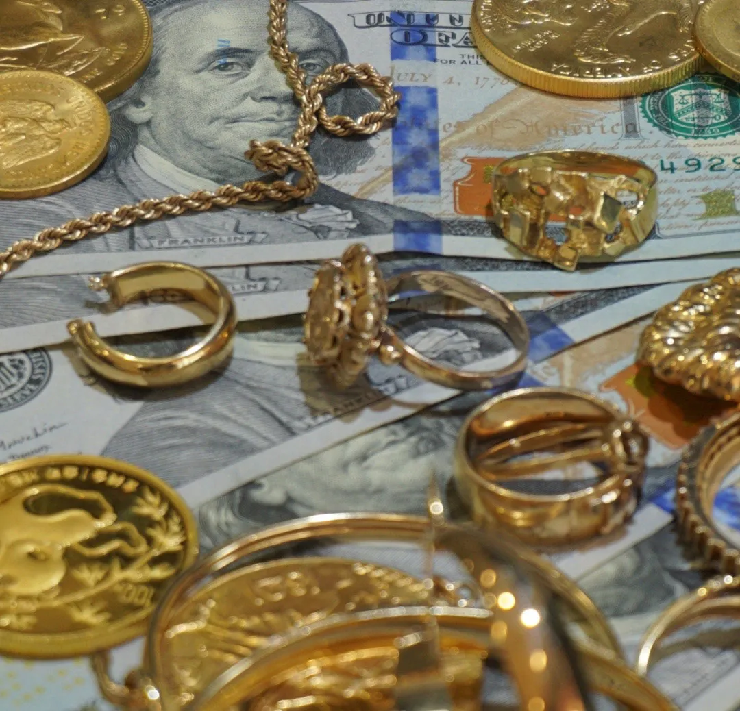 Gold jewelry and coins laying on hundred dollar bills