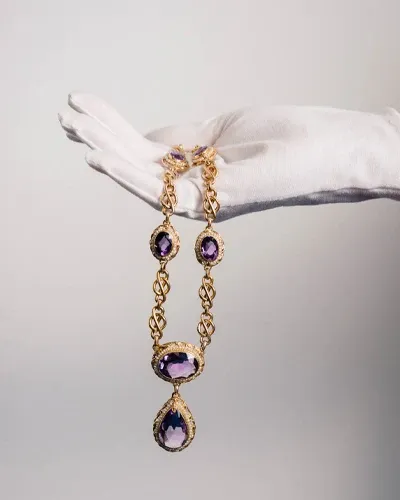 A gloved hand holding an antique gold and amethyst estate necklace during an appraisal