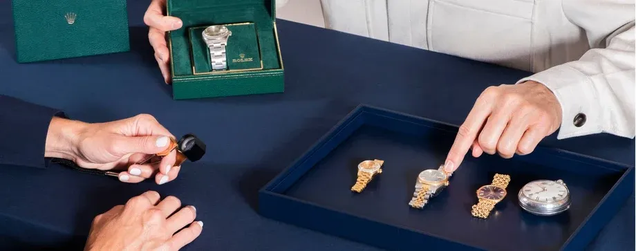 A National Rarities estate specialist examining watches with a loupe while a customer looks over a tray of gold watches at Morin Jewelers