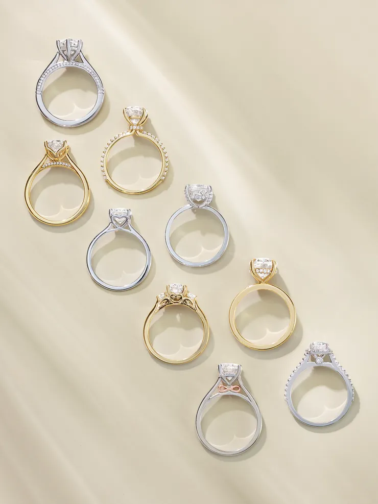 Nine diamond engagement rings in white and yellow gold standing upright on a cream surface