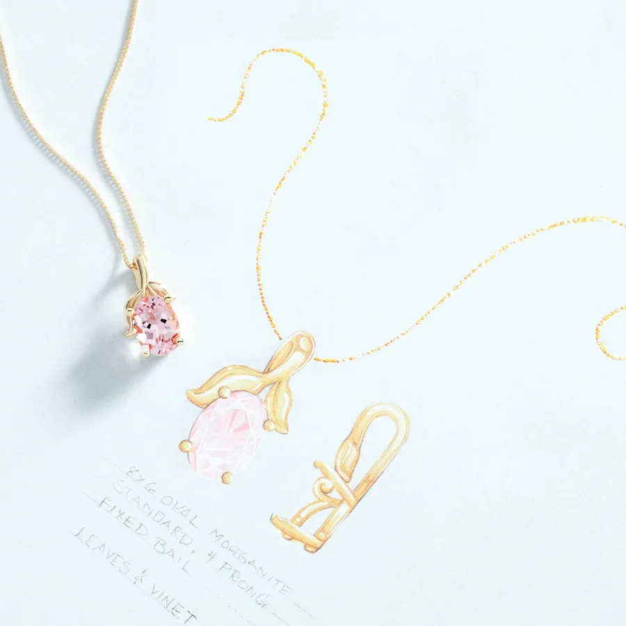 A gold and morganite pendant resting on the annotated design drawing it was made from, noting the oval stone size, four-prong setting, fixed bail and leaves-and-vine detail