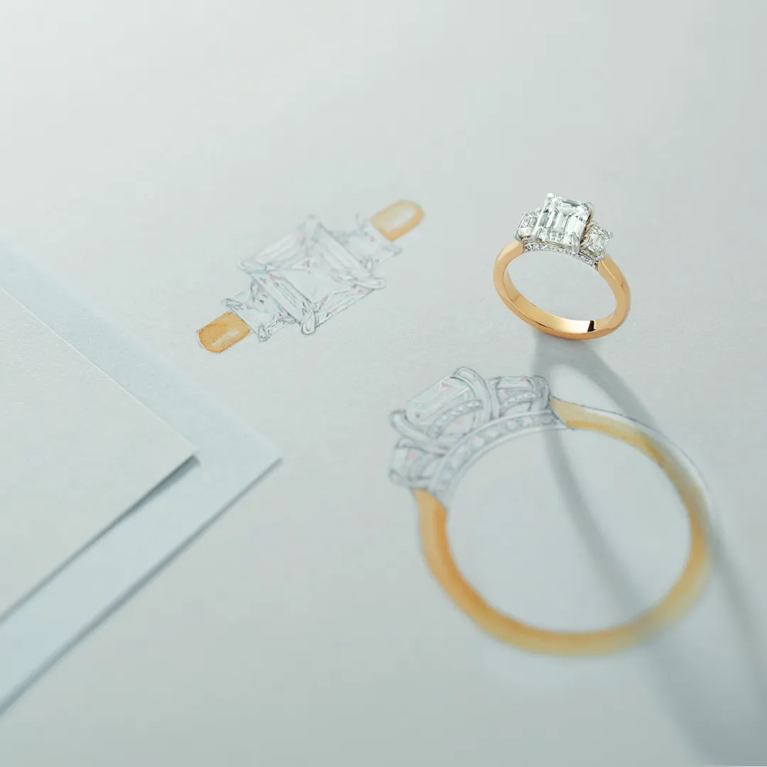 A finished gold and diamond three-stone ring standing on the hand-drawn design it was made from at Morin Jewelers in Southbridge, MA