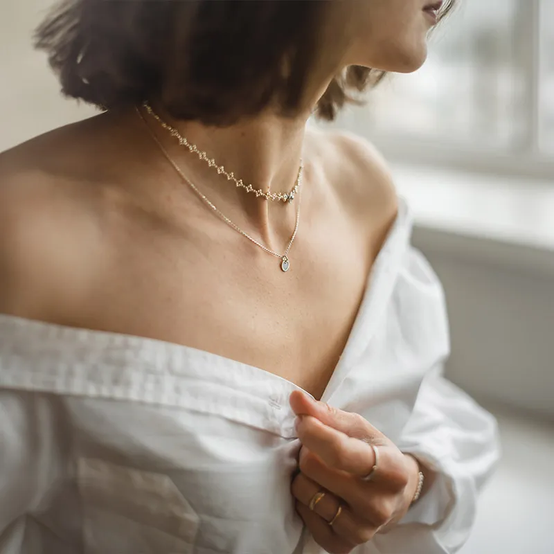 Woman in white shirt wearing layered necklaces and rings, showcasing jewelry from Morin Jewelers.