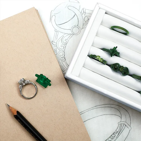 A ring design sketch beside wax models and a finished ring