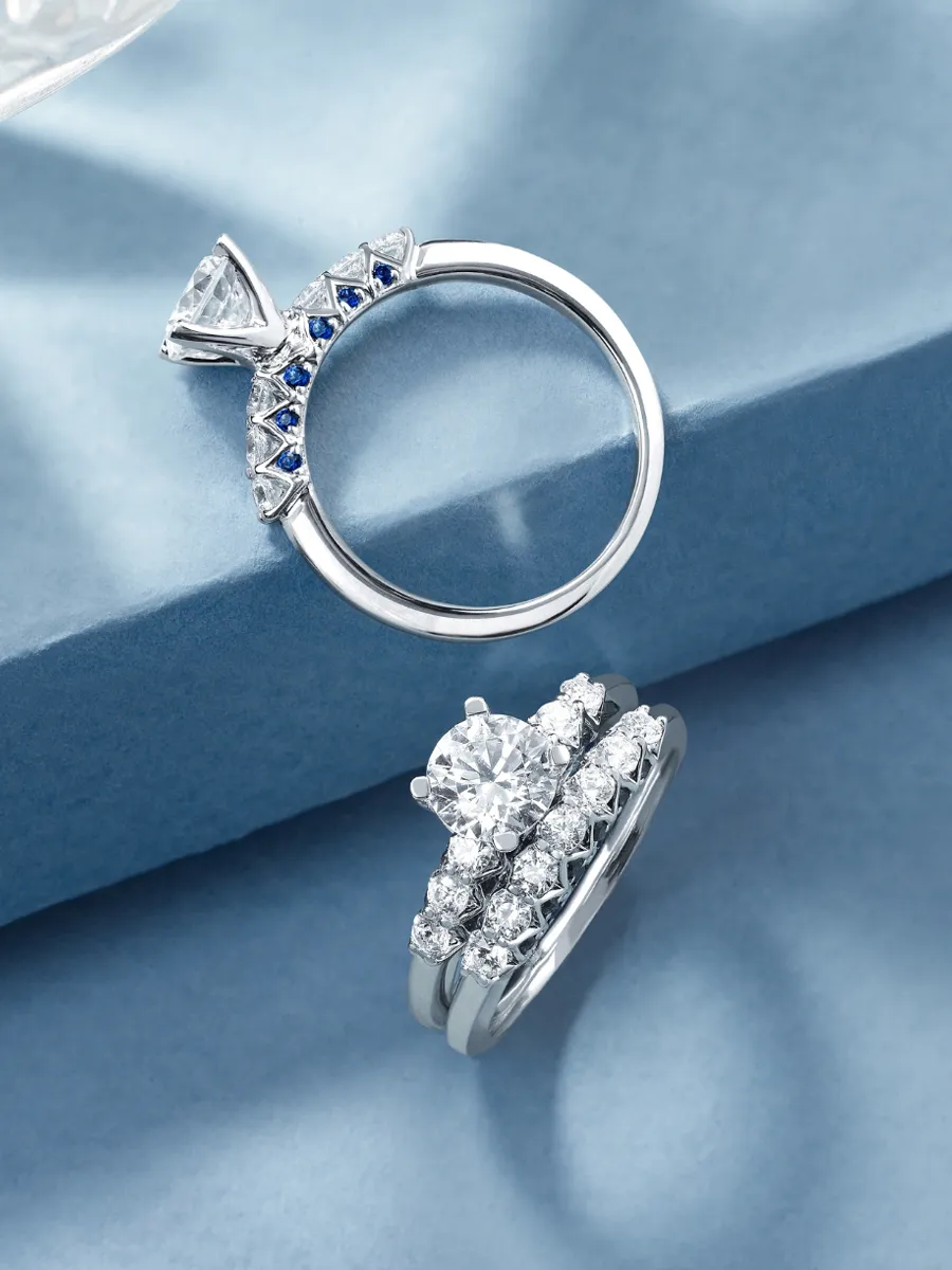 Elegant engagement and wedding rings featuring diamonds and sapphires, displayed on a soft blue background.