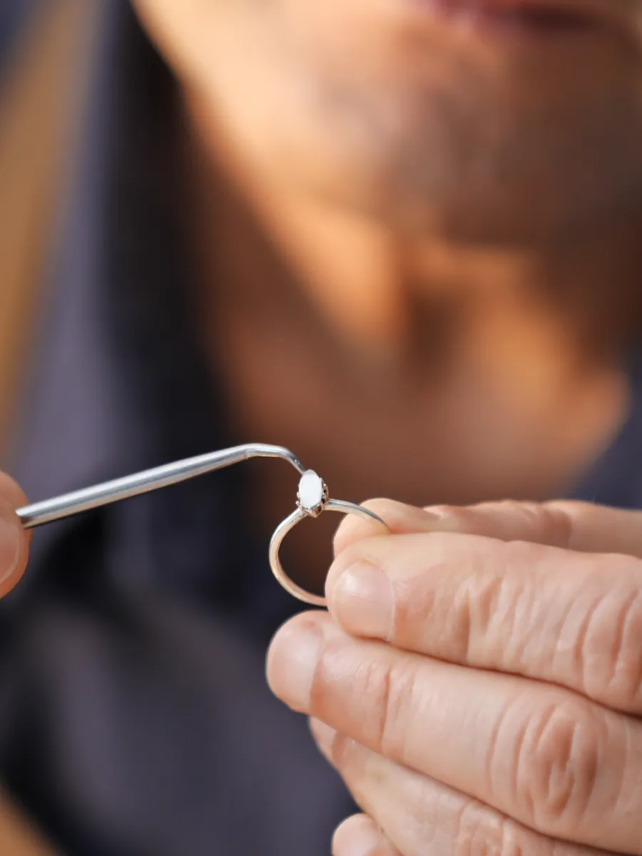 Jeweler holding a ring with a gemstone, using a tool for adjustment.