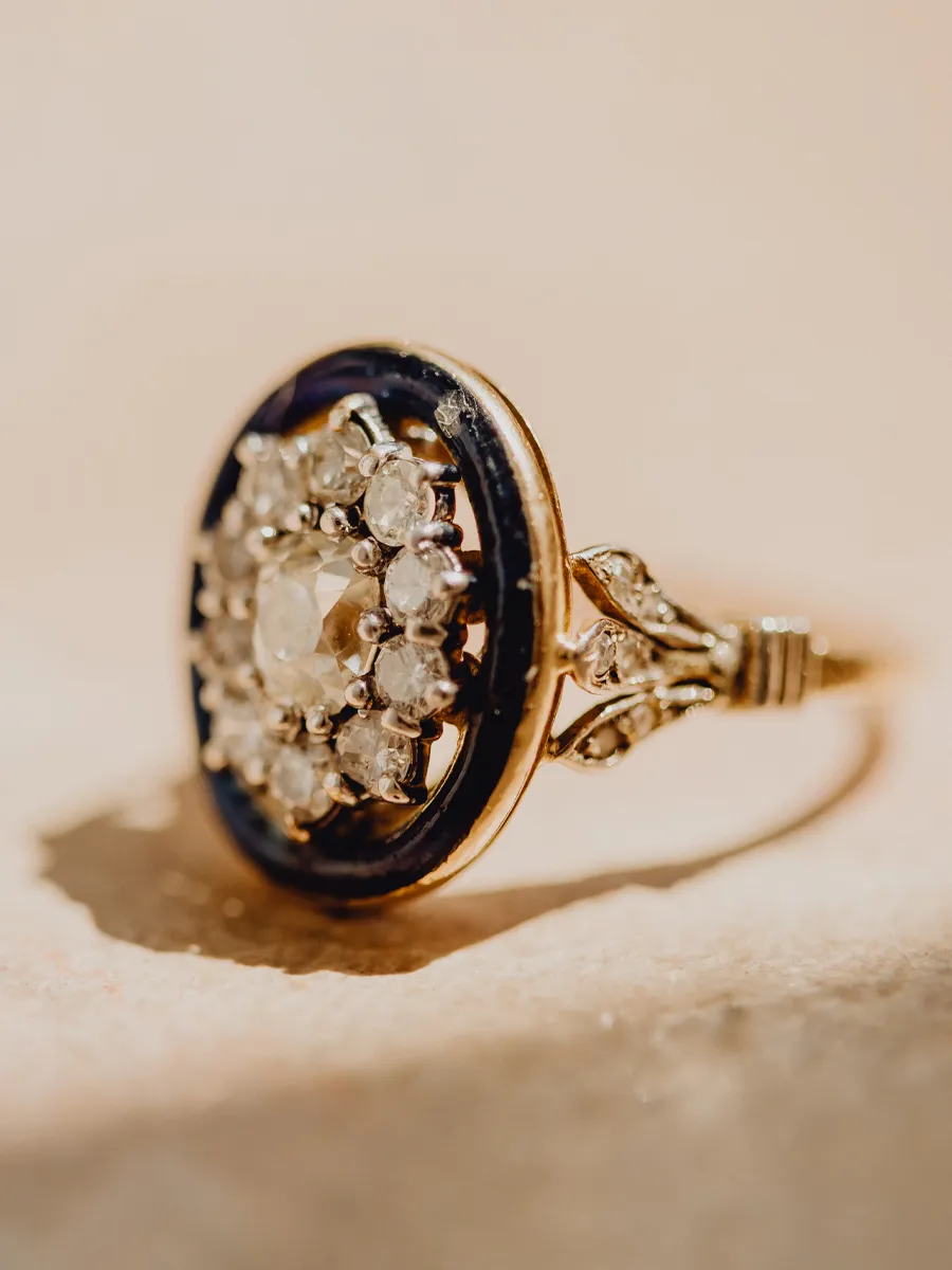 Vintage gold ring with a central diamond and surrounding smaller stones, set against a light background.