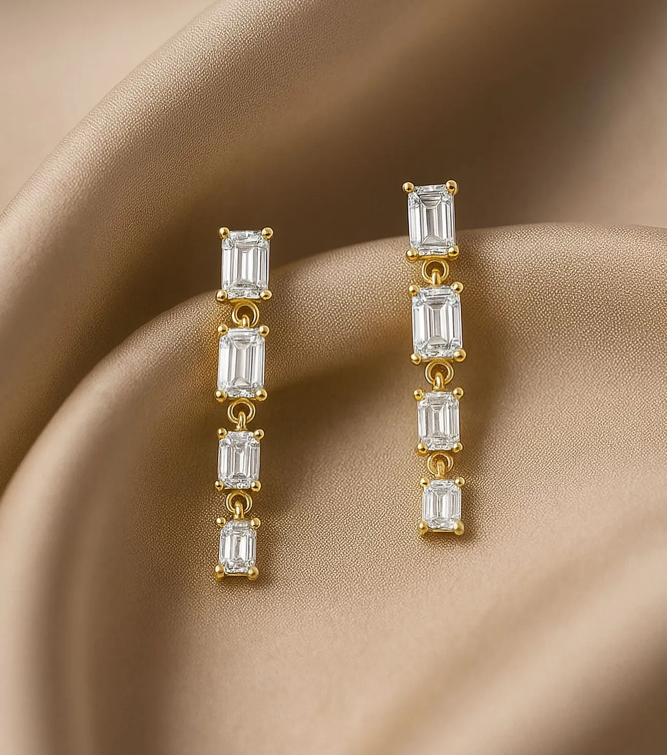 Elegant gold earrings with clear rectangular stones, displayed on soft beige fabric.