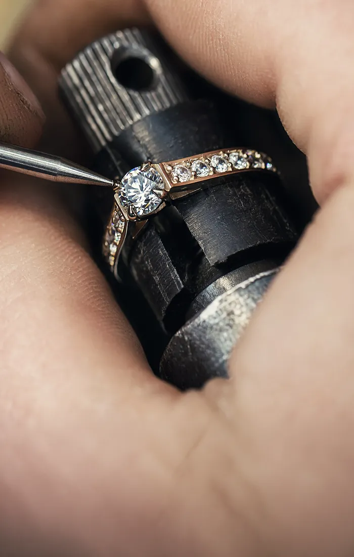 A rose gold engagement ring with an oval diamond and pavé band on a marble surface.