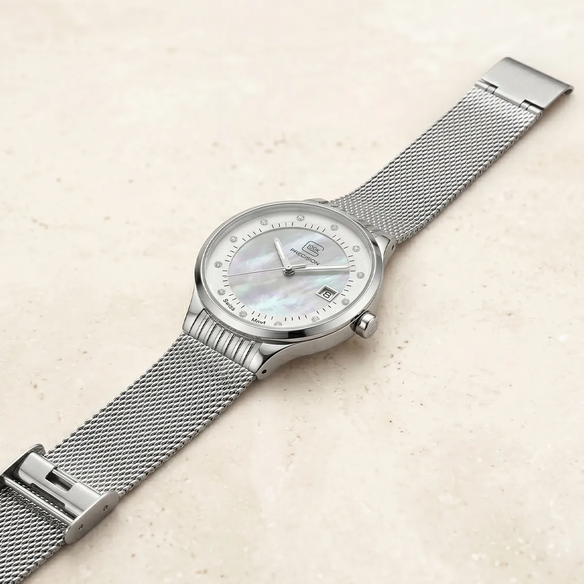 Silver mesh strap watch with a mother-of-pearl dial on a light surface. Explore estate jewelry at Pearce Jewelers.